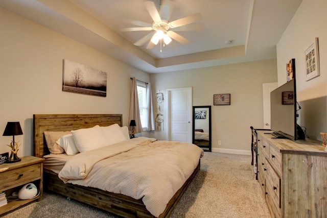 carpeted bedroom with ceiling fan and a raised ceiling