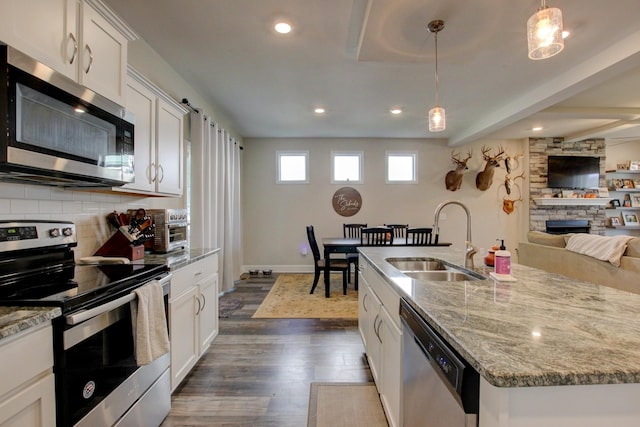 kitchen with appliances with stainless steel finishes, sink, decorative light fixtures, a center island with sink, and white cabinets