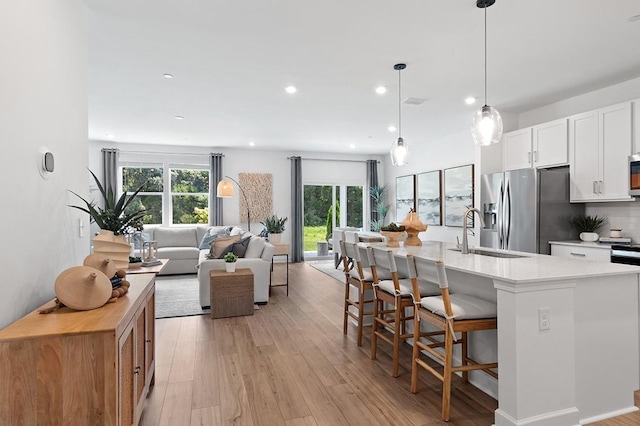 kitchen featuring stainless steel refrigerator with ice dispenser, sink, decorative light fixtures, white cabinetry, and an island with sink