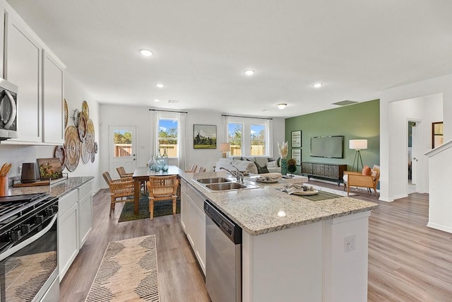 kitchen with light stone countertops, appliances with stainless steel finishes, sink, a center island with sink, and white cabinetry