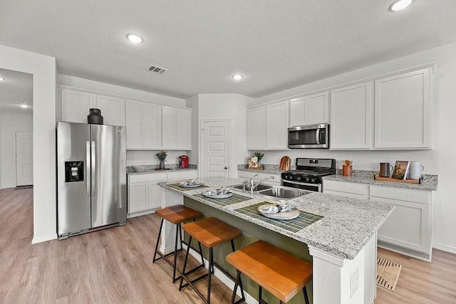 kitchen featuring white cabinets, sink, stainless steel appliances, and an island with sink