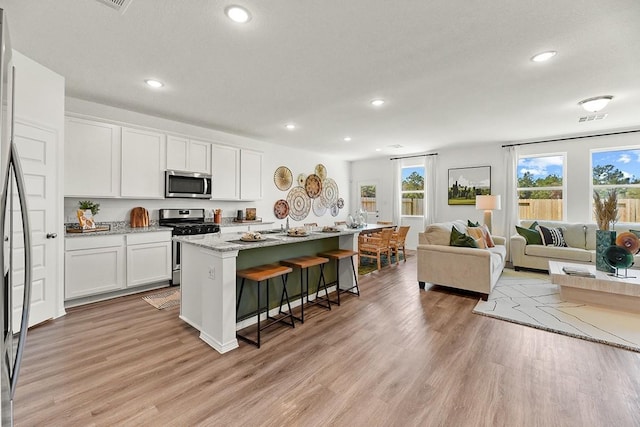 kitchen featuring a kitchen island with sink, white cabinets, a kitchen breakfast bar, light wood-type flooring, and appliances with stainless steel finishes