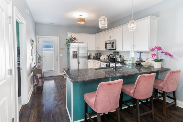 kitchen featuring kitchen peninsula, appliances with stainless steel finishes, sink, white cabinets, and hanging light fixtures