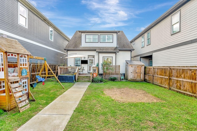 back of house featuring a playground, a wooden deck, and a lawn