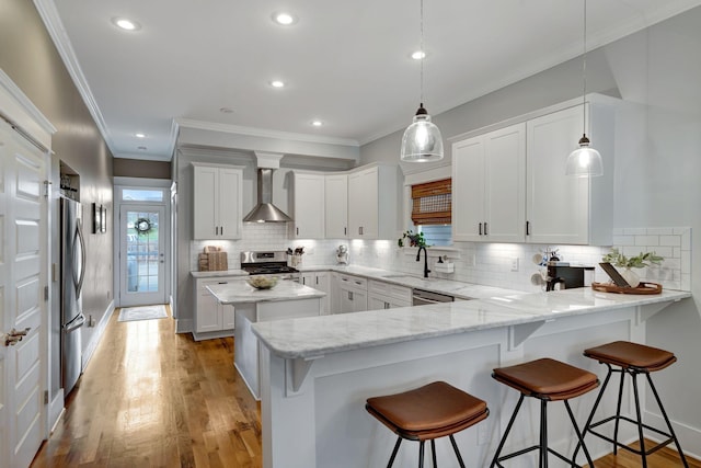 kitchen featuring kitchen peninsula, appliances with stainless steel finishes, white cabinets, and wall chimney exhaust hood