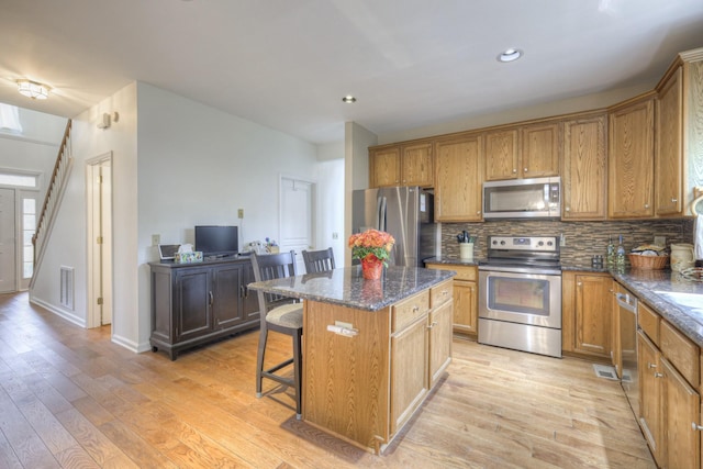 kitchen with a kitchen breakfast bar, a center island, stainless steel appliances, and light hardwood / wood-style floors