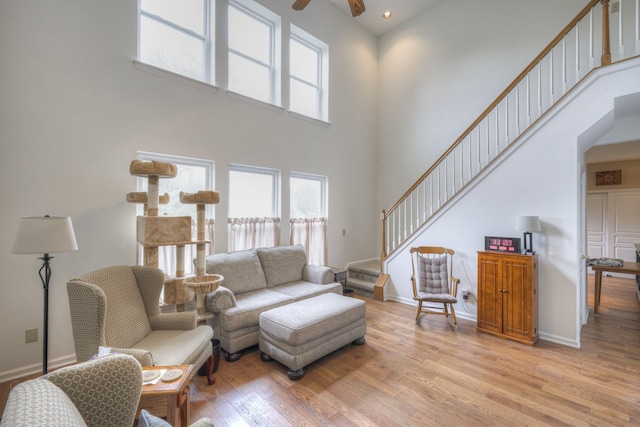 living room with ceiling fan, light wood-type flooring, and a high ceiling