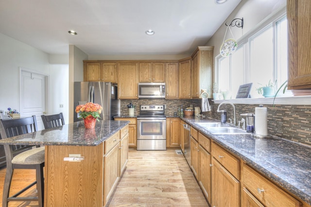 kitchen with sink, light hardwood / wood-style flooring, a kitchen bar, a kitchen island, and appliances with stainless steel finishes