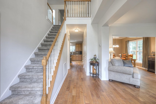 stairs with hardwood / wood-style flooring, ornamental molding, and a chandelier