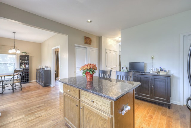 kitchen with dark stone counters, decorative light fixtures, light hardwood / wood-style flooring, an inviting chandelier, and a kitchen island