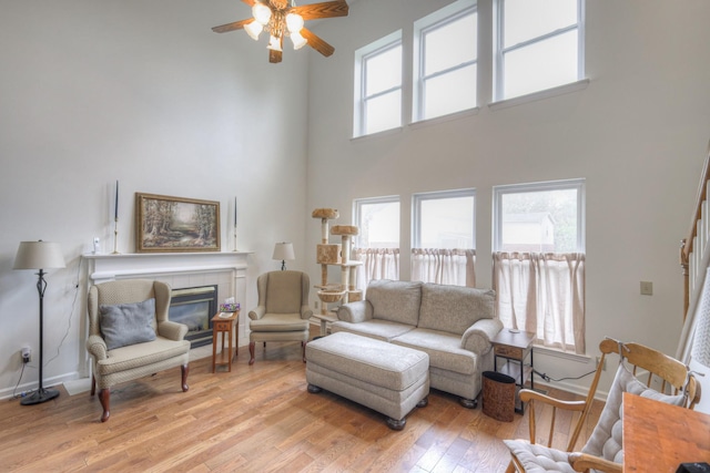 living room with ceiling fan, a tile fireplace, a high ceiling, and light hardwood / wood-style flooring