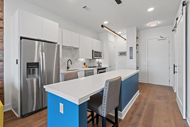 kitchen with white cabinetry, a barn door, decorative light fixtures, a kitchen island, and appliances with stainless steel finishes