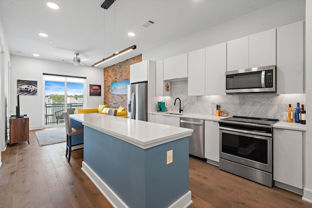 kitchen with white cabinetry, sink, hanging light fixtures, stainless steel appliances, and a kitchen island