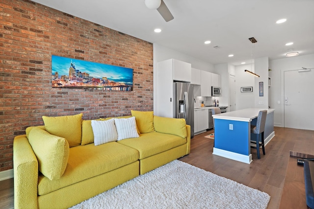 living room with ceiling fan, dark wood-type flooring, and brick wall