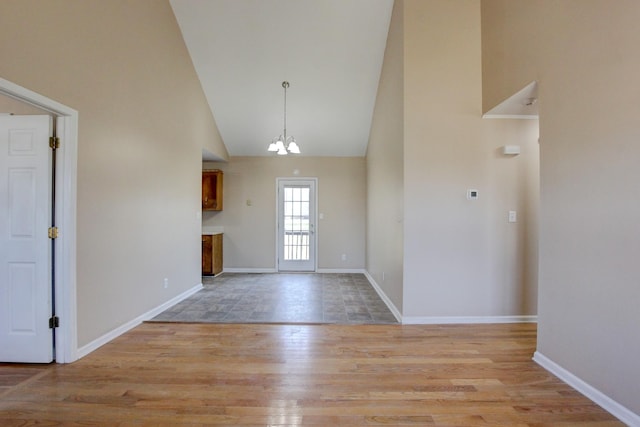 foyer entrance featuring a notable chandelier, baseboards, light wood-type flooring, and high vaulted ceiling