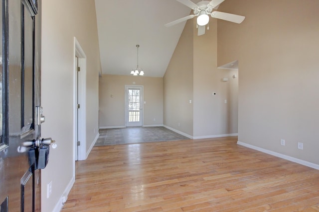 spare room featuring baseboards, ceiling fan with notable chandelier, light wood-type flooring, and high vaulted ceiling