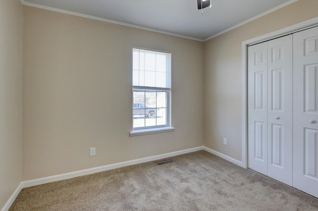 unfurnished bedroom with baseboards, visible vents, carpet floors, a closet, and crown molding