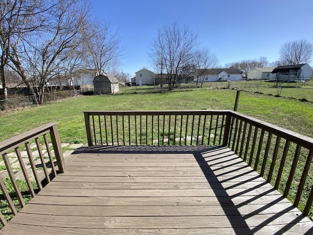 wooden deck featuring a storage unit, an outbuilding, a lawn, a fenced backyard, and a residential view