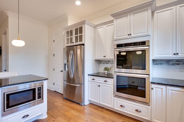 kitchen with light wood-style flooring, white cabinets, hanging light fixtures, appliances with stainless steel finishes, and backsplash