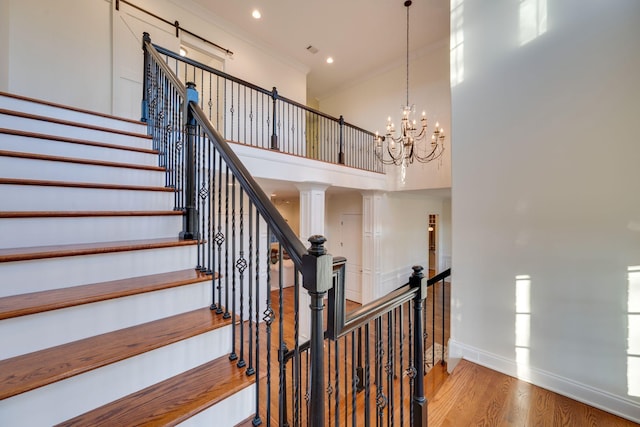 staircase with baseboards, wood finished floors, a high ceiling, crown molding, and a notable chandelier