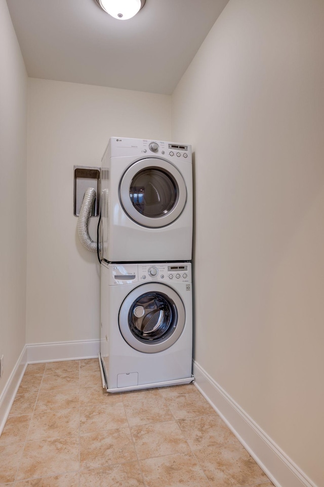 clothes washing area with stacked washer / drying machine, laundry area, baseboards, and light tile patterned floors