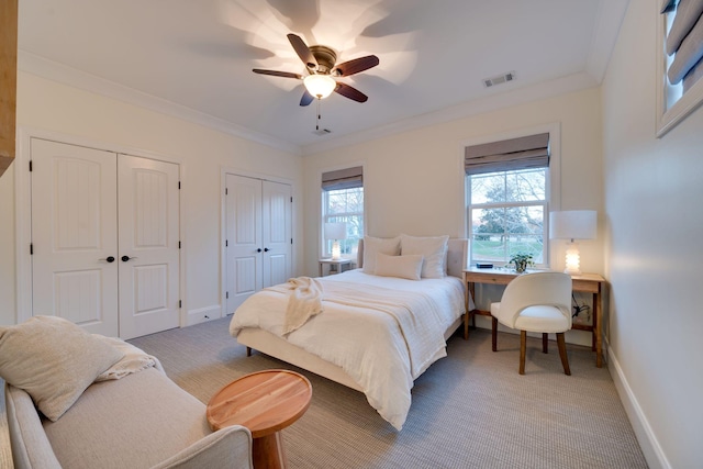 bedroom featuring carpet floors, visible vents, baseboards, multiple closets, and ornamental molding