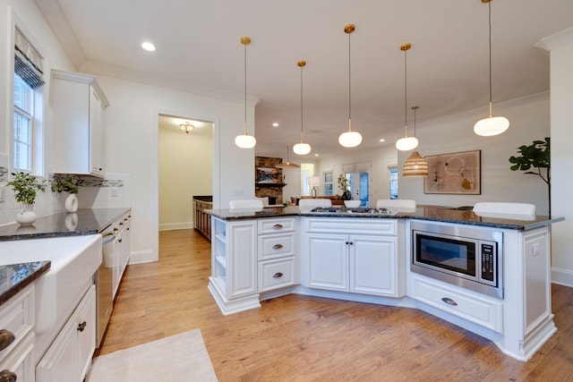 kitchen featuring stainless steel appliances, light wood-style floors, white cabinets, hanging light fixtures, and backsplash