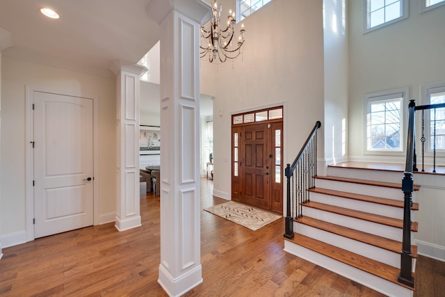 entryway featuring a notable chandelier, decorative columns, a high ceiling, light wood-type flooring, and stairs