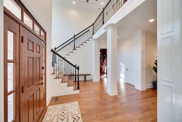 foyer entrance featuring light wood-style floors, decorative columns, a towering ceiling, and stairs