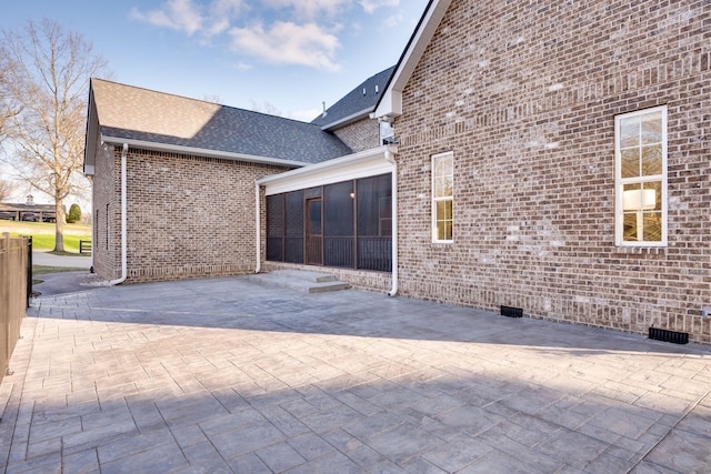 view of home's exterior featuring a sunroom, roof with shingles, a patio area, and brick siding