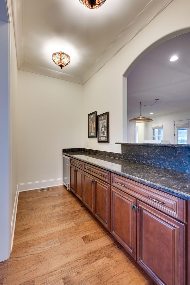 kitchen with arched walkways, visible vents, light wood-style floors, ornamental molding, and dark stone countertops