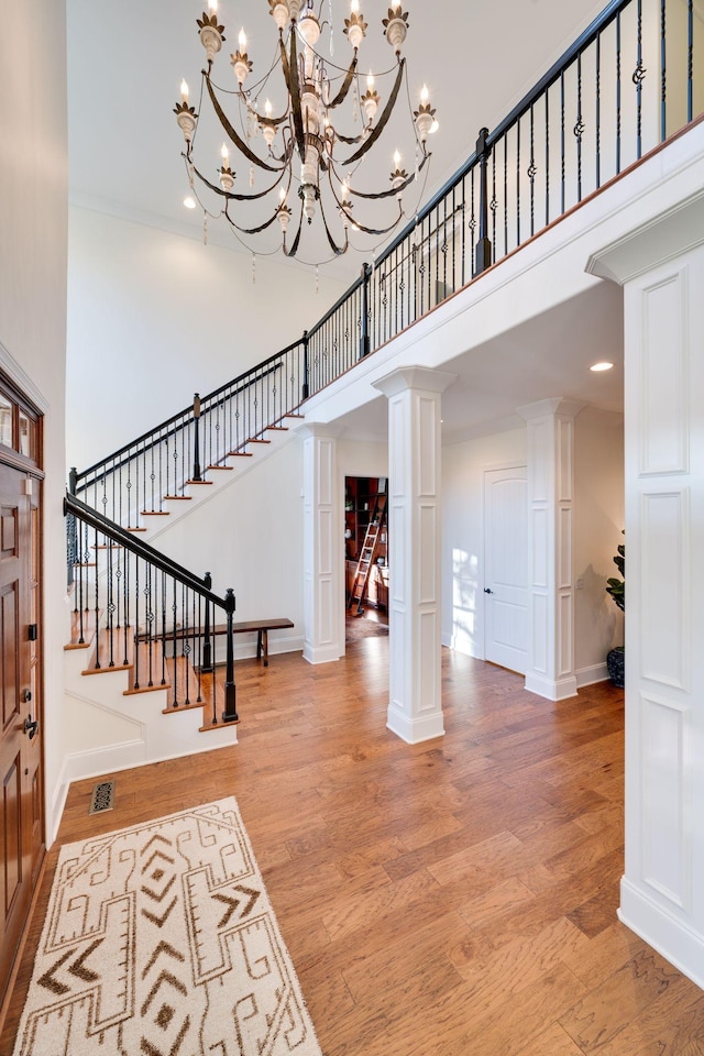 entrance foyer featuring decorative columns, visible vents, stairway, wood finished floors, and a high ceiling