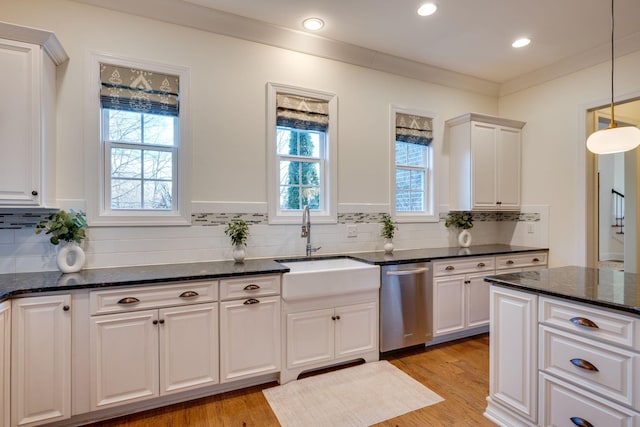 kitchen featuring hanging light fixtures, stainless steel dishwasher, a sink, and white cabinetry