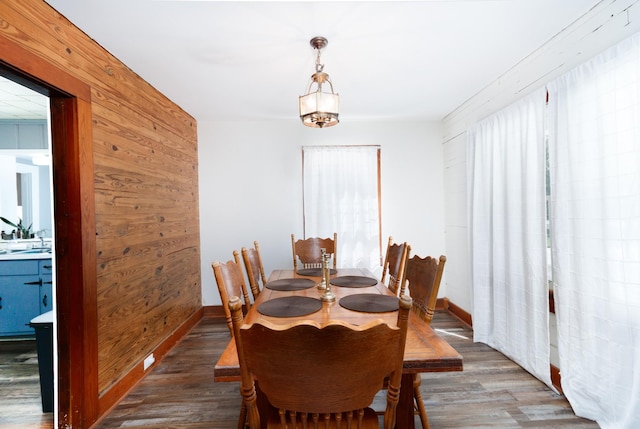 dining space with wood walls and dark wood-type flooring