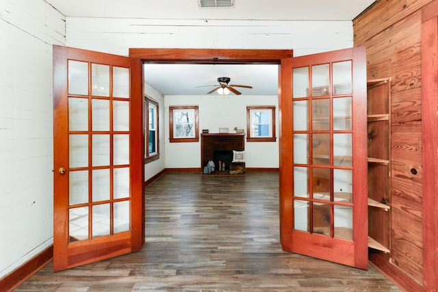 doorway with a brick fireplace, ceiling fan, wooden walls, and french doors