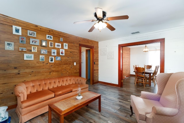 living room with dark hardwood / wood-style flooring, ceiling fan, and wood walls