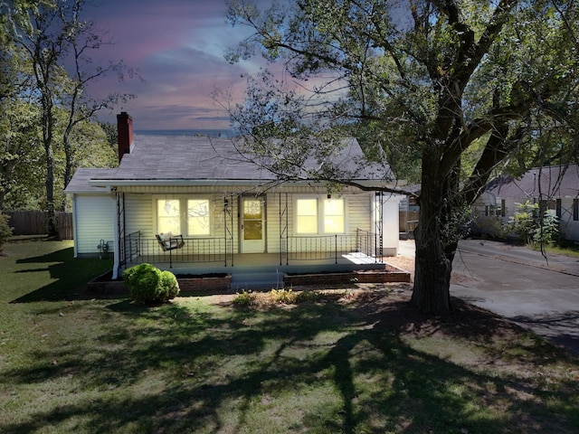 back house at dusk featuring covered porch and a lawn