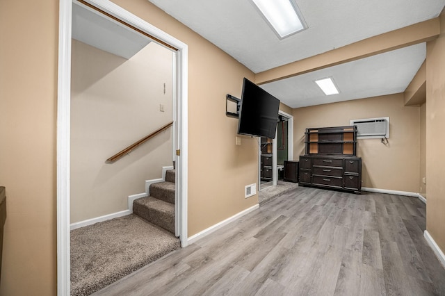 basement with a wall mounted air conditioner and light hardwood / wood-style flooring