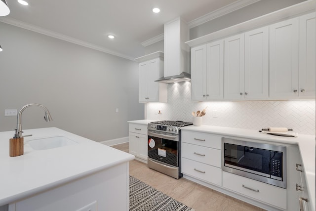 kitchen with white cabinetry, sink, wall chimney range hood, appliances with stainless steel finishes, and ornamental molding