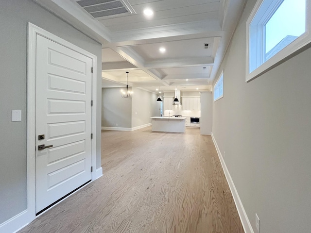 unfurnished living room featuring coffered ceiling, beamed ceiling, a notable chandelier, crown molding, and light hardwood / wood-style floors