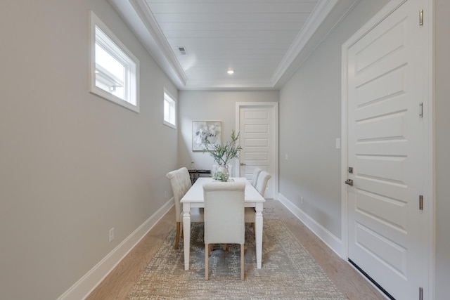 dining room with light hardwood / wood-style floors, a raised ceiling, and crown molding