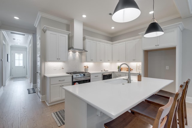 kitchen featuring white cabinets, wall chimney exhaust hood, a center island with sink, and stainless steel gas range