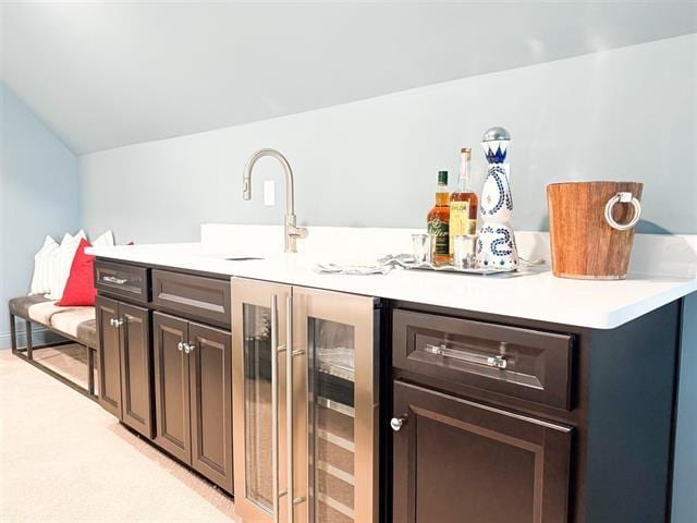 interior space with vaulted ceiling, dark brown cabinetry, beverage cooler, and sink