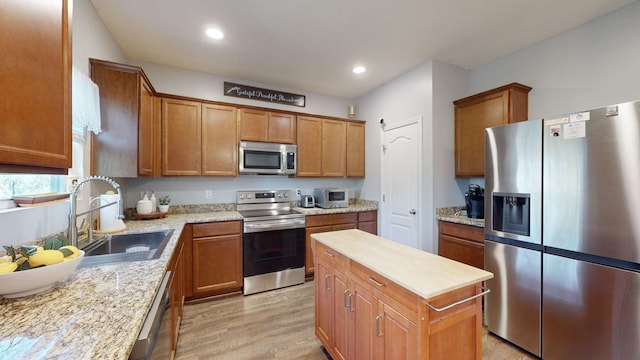 kitchen featuring a center island, sink, light wood-type flooring, stainless steel appliances, and light stone counters