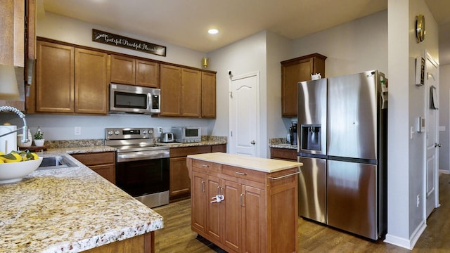 kitchen featuring light stone countertops, appliances with stainless steel finishes, a kitchen island, dark hardwood / wood-style flooring, and sink