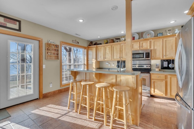 kitchen with a breakfast bar, light brown cabinets, sink, a kitchen island, and stainless steel appliances