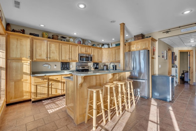 kitchen with sink, stainless steel appliances, a kitchen breakfast bar, an island with sink, and light brown cabinetry