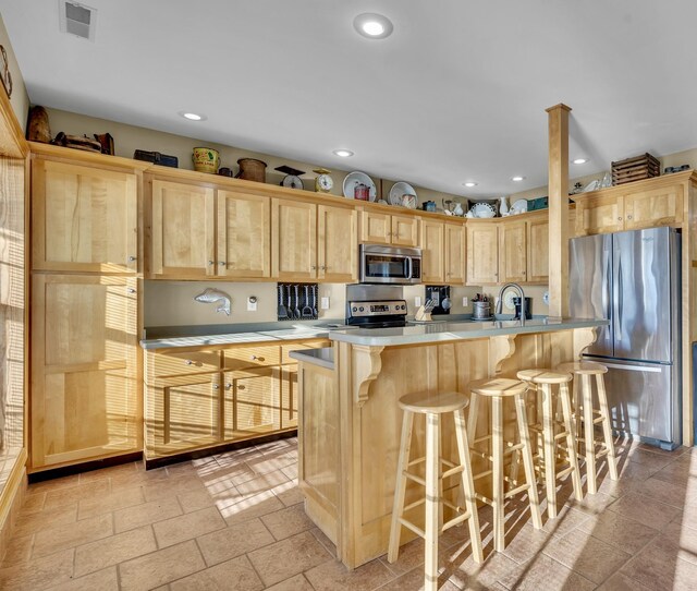 kitchen with light brown cabinets, visible vents, stainless steel appliances, light countertops, and a kitchen bar