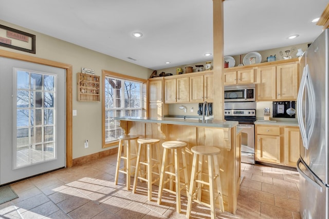 kitchen with light brown cabinets, recessed lighting, stainless steel appliances, a breakfast bar, and light countertops