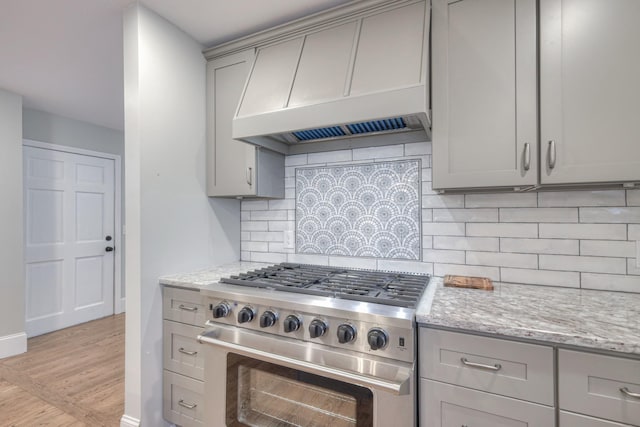 kitchen featuring light stone counters, custom range hood, high end stainless steel range oven, and tasteful backsplash